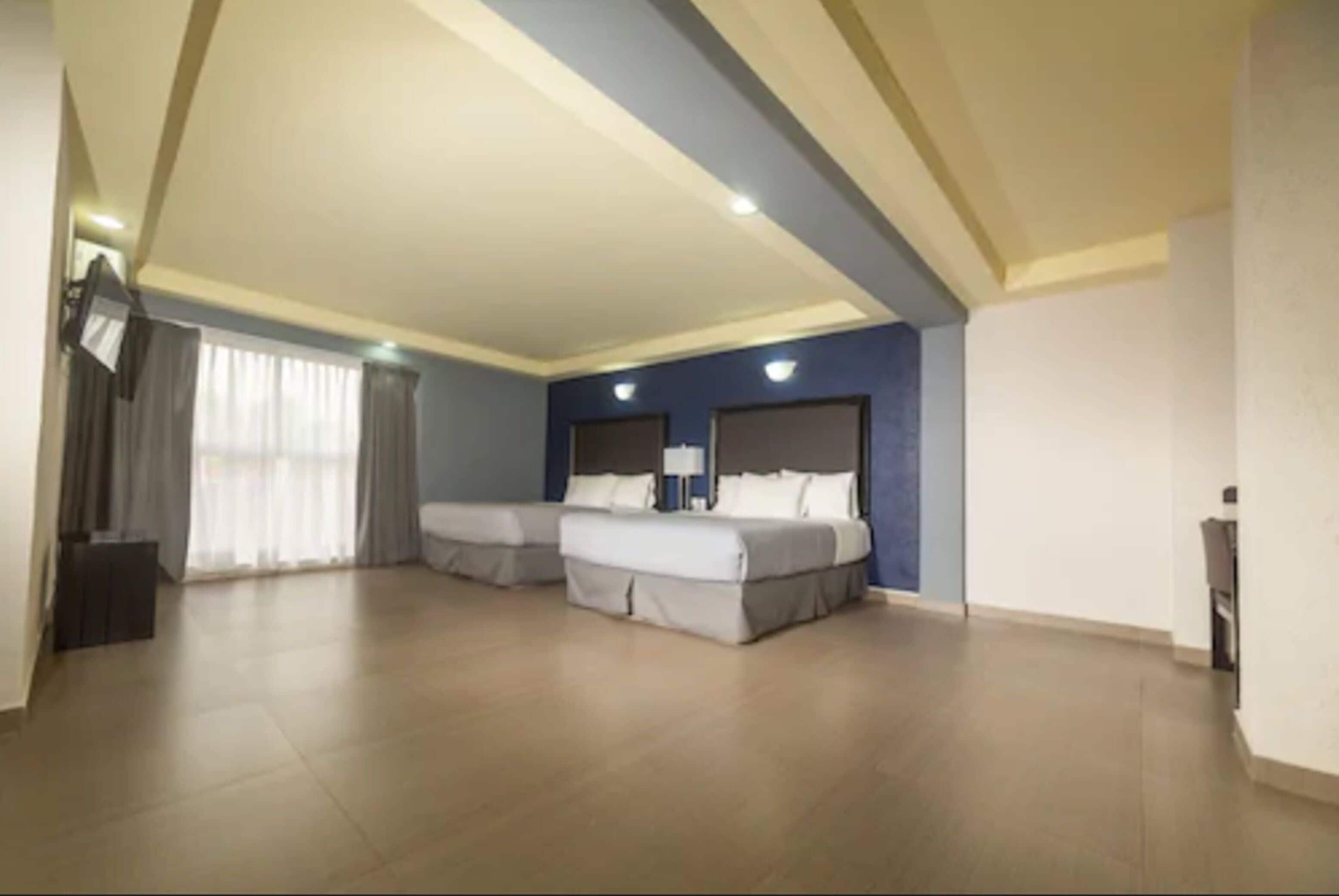 Une chambre d’hôtel spacieuse, dotée de deux lits, d’une grande fenêtre avec des rideaux et d’un téléviseur à écran plat.