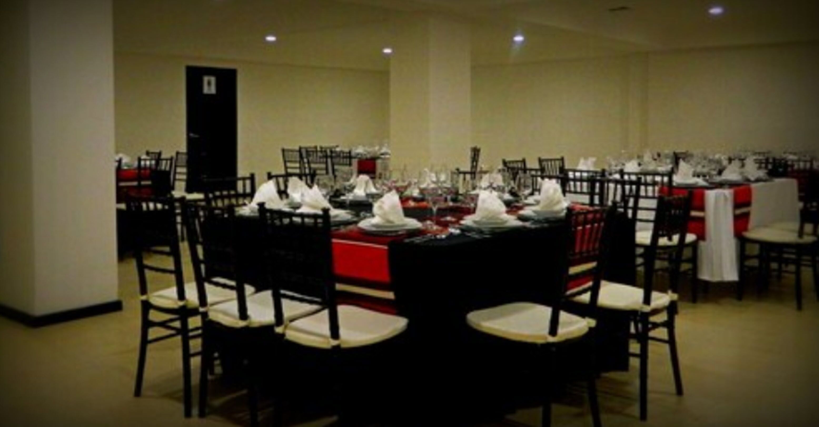A banquet hall with round tables set for a formal event, each with white tablecloths and red centerpieces.