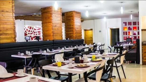 A restaurant with multiple tables and chairs, a black booth seating area, and brick pillars. - Hotel Ha (Orizaba)