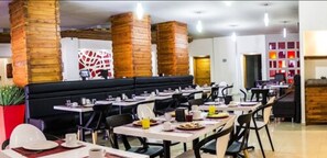 A restaurant with multiple tables and chairs, a black booth seating area, and brick pillars. - Hotel Ha (Orizaba)