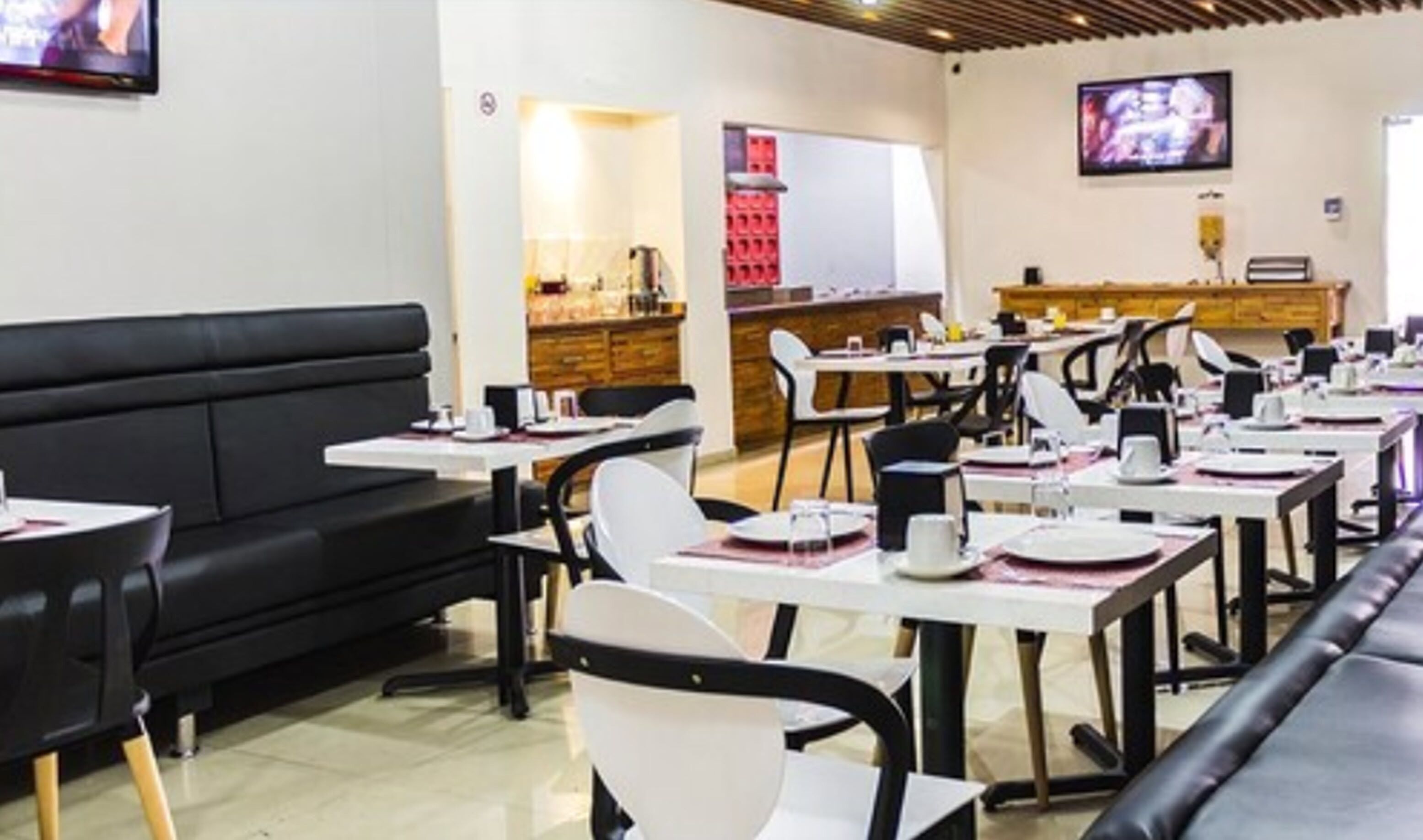 Um restaurante com um sofá preto, cadeiras brancas e mesas preparadas para refeições.