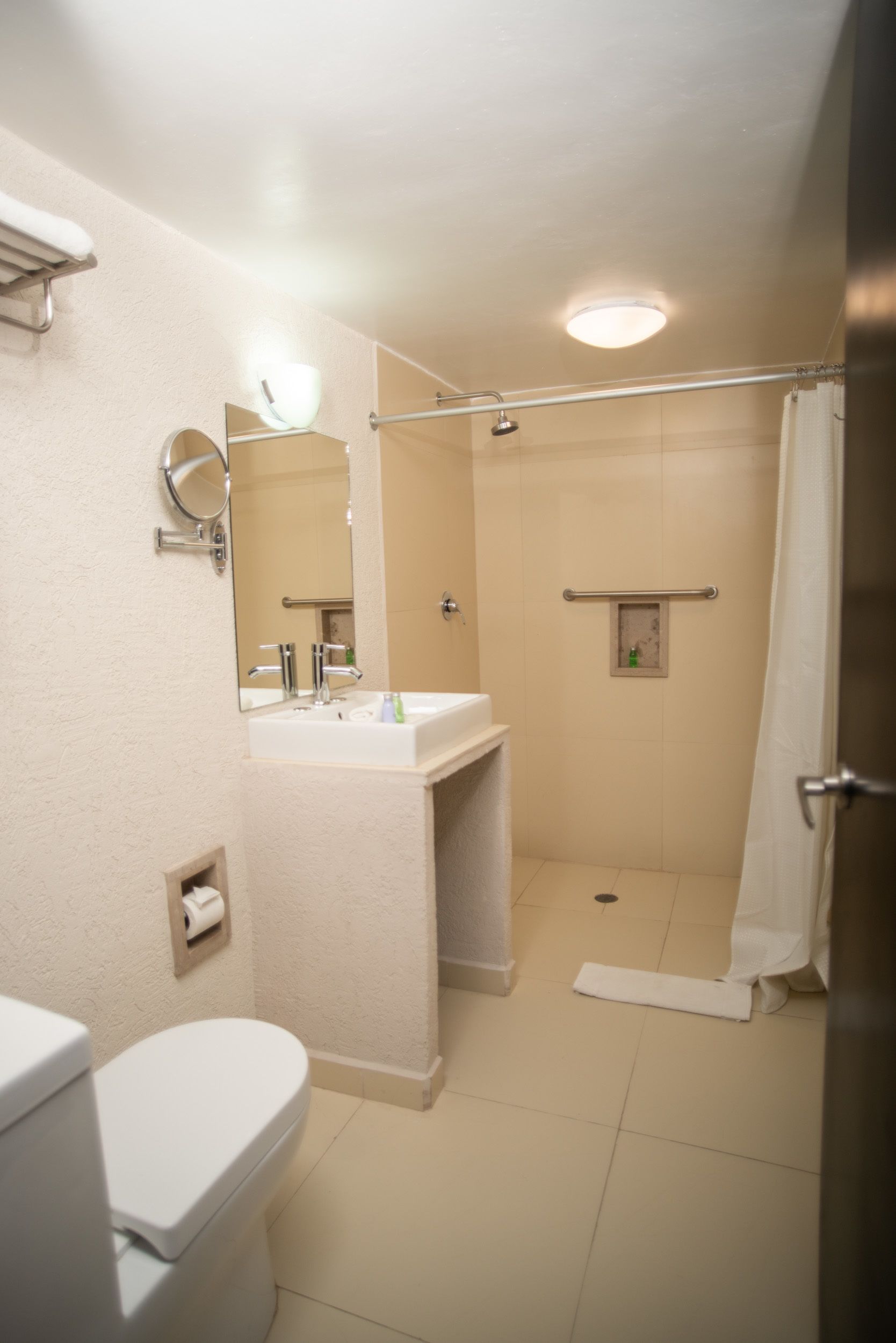 A bathroom with a toilet, sink, mirror, shower, and a towel rack.