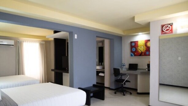 A hotel room with a bed, a desk, a chair, and a painting on the wall. - Hotel Ha (Orizaba)