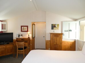 A hotel room with a bed, desk, chair, television, and a mirror. - Carmel Fireplace Inn (Carmel)