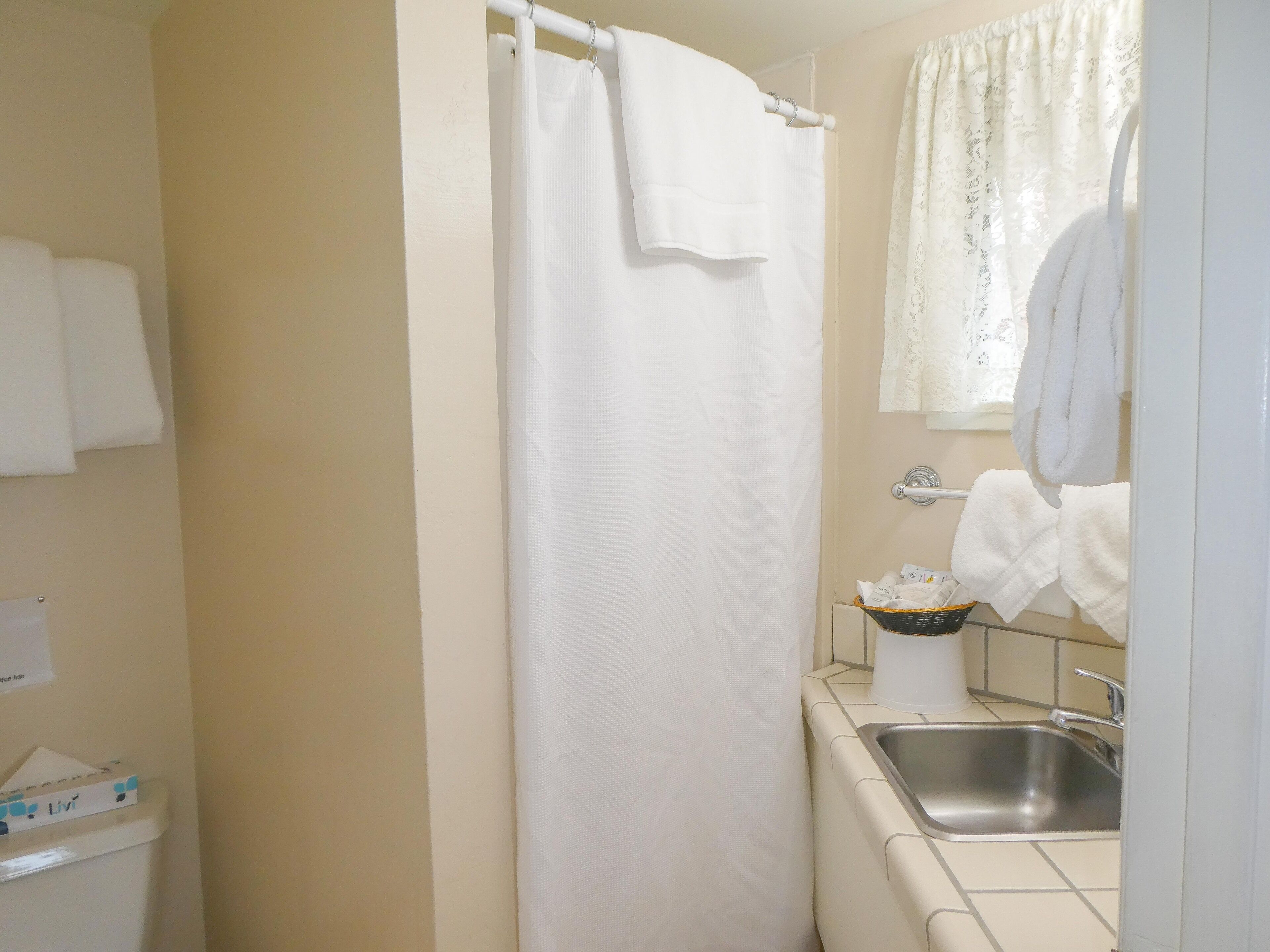 A bathroom with a shower curtain, a sink, and a window with a curtain.