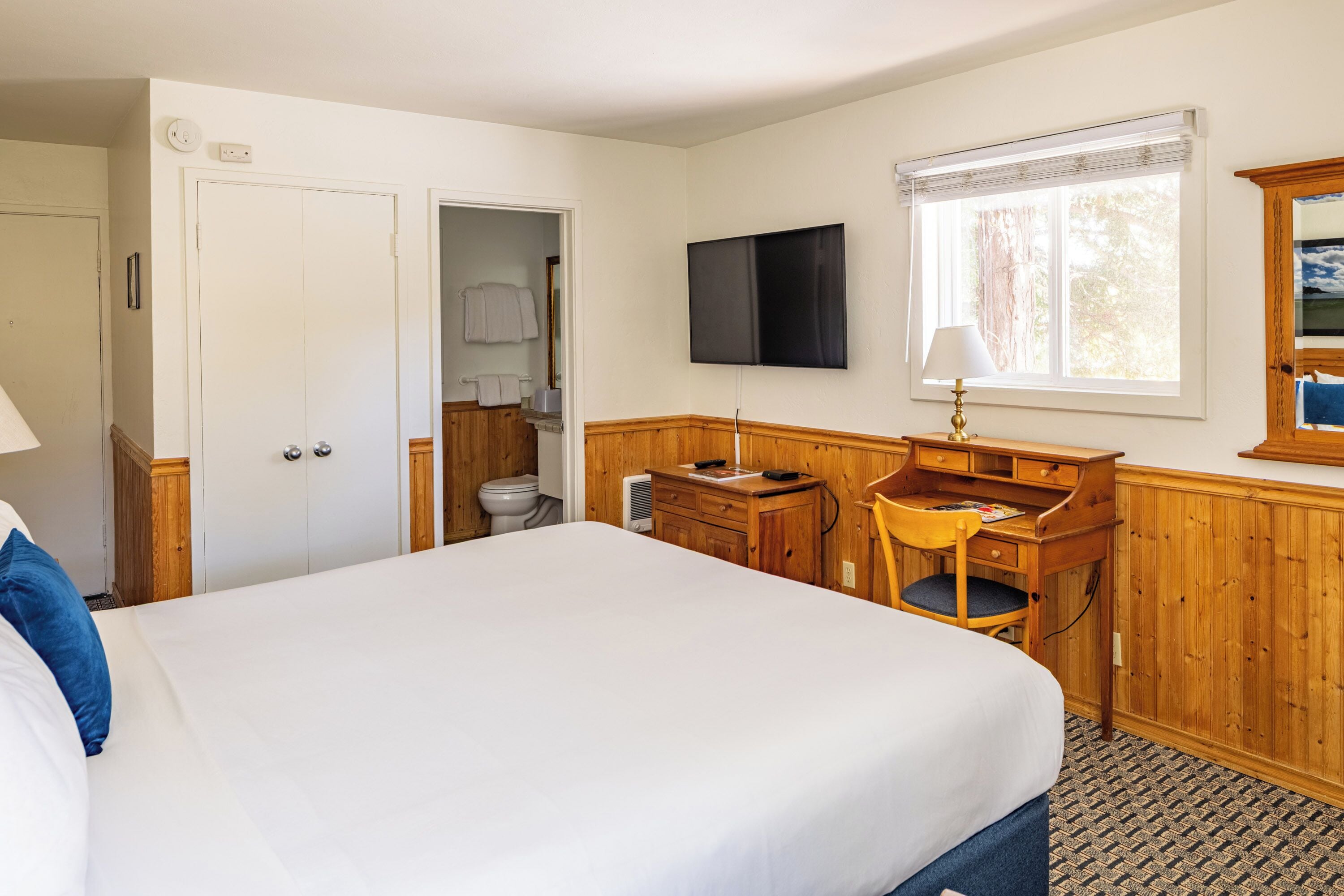 Un dormitorio con una cama grande, un escritorio de madera, un televisor y una ventana con persianas.
