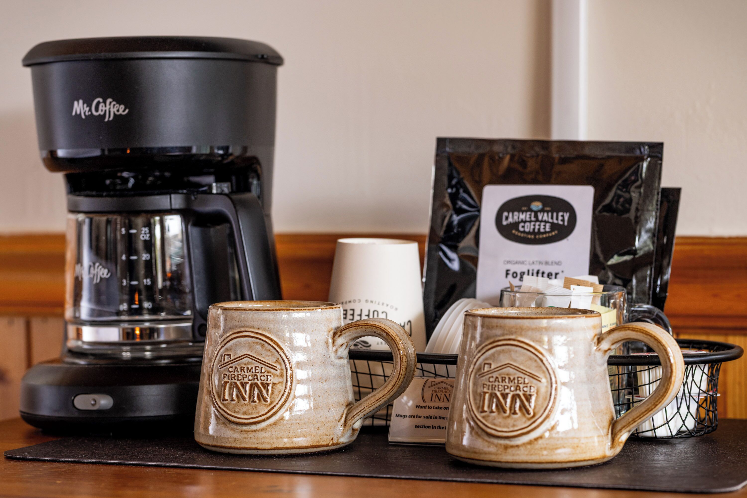 Une machine à café, deux tasses, un paquet de café et une enseigne pour Carmel Valley Coffee.