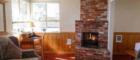 A cozy room with a brick fireplace, patterned furniture, and a window with blinds.
