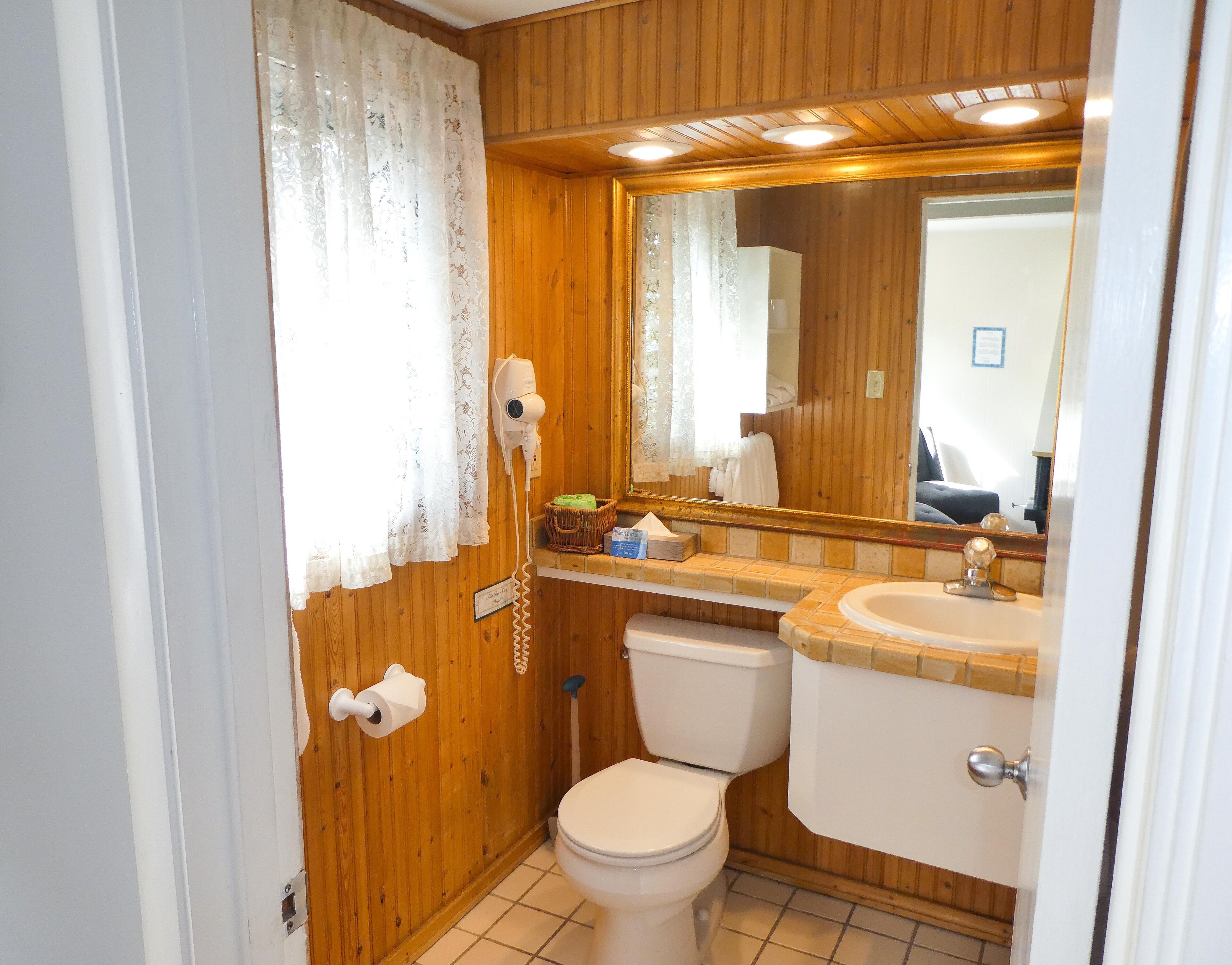 Une petite salle de bain avec des murs en bois, des toilettes, un lavabo, un miroir et un sèche-cheveux.