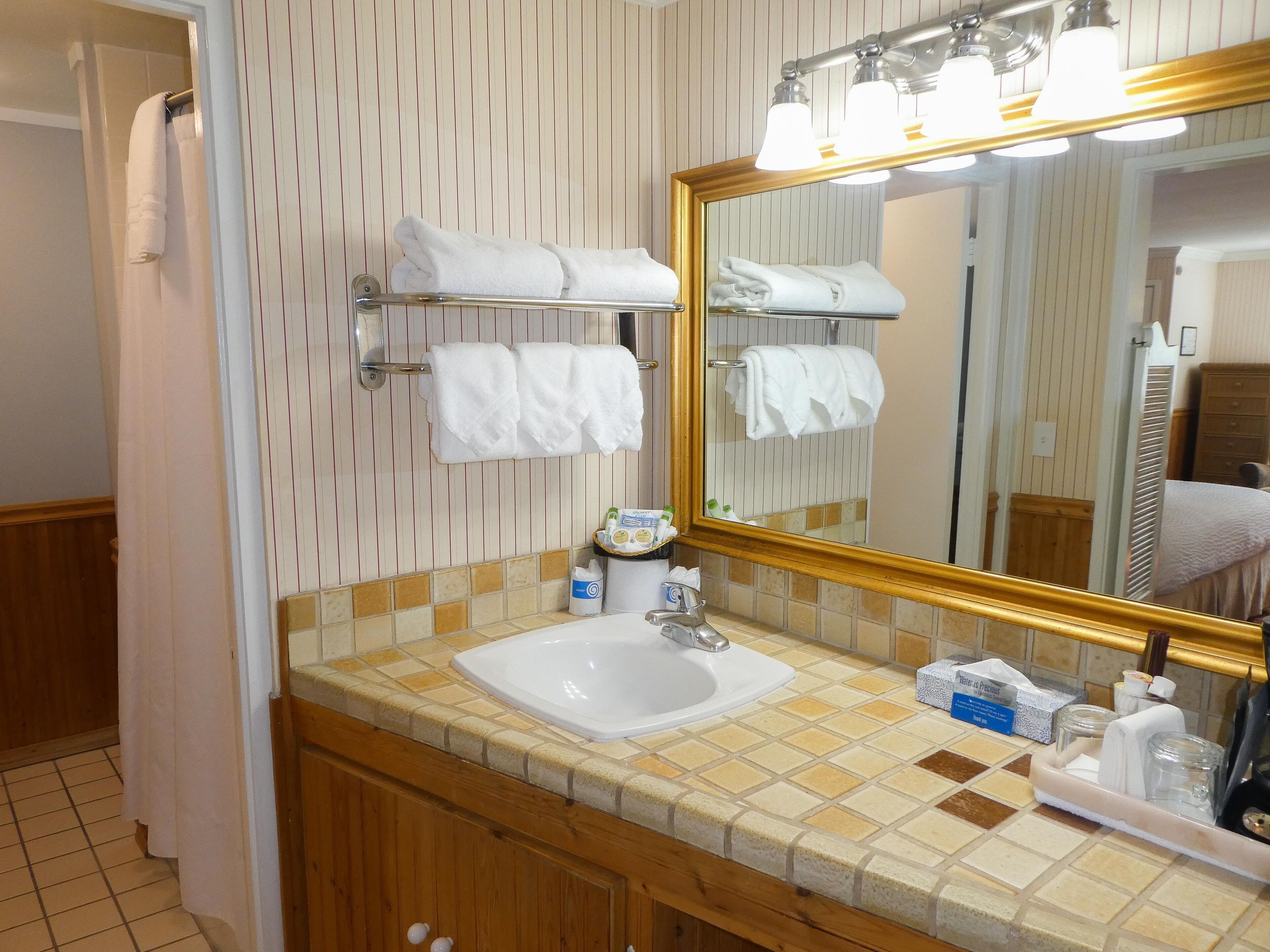 A bathroom with a sink, mirror, towel rack, and toiletries.