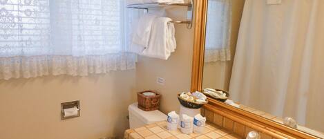 A bathroom with a toilet, sink, and a large mirror. There are towels hanging on a rack and a basket with toiletries on the sink.