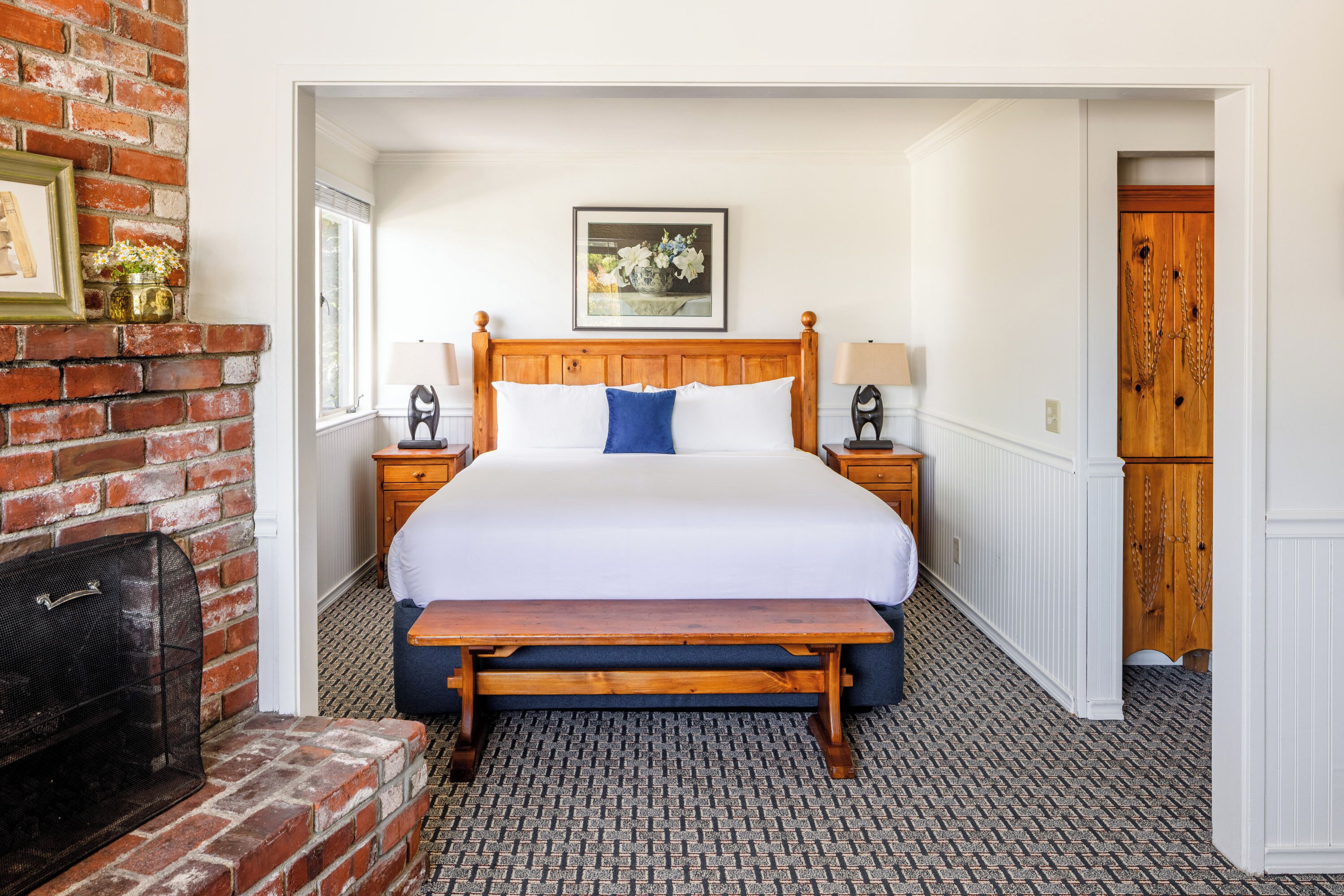 A bedroom with a wooden bed, a bench, a fireplace, and a framed picture on the wall.