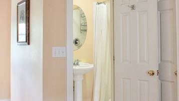 Un pasillo que conduce a un baño con lavamanos blanco, espejo y cortina de ducha.