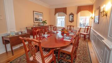 Une salle à manger avec une table ronde en bois, six chaises, un centre de table floral et un tapis à motifs.
