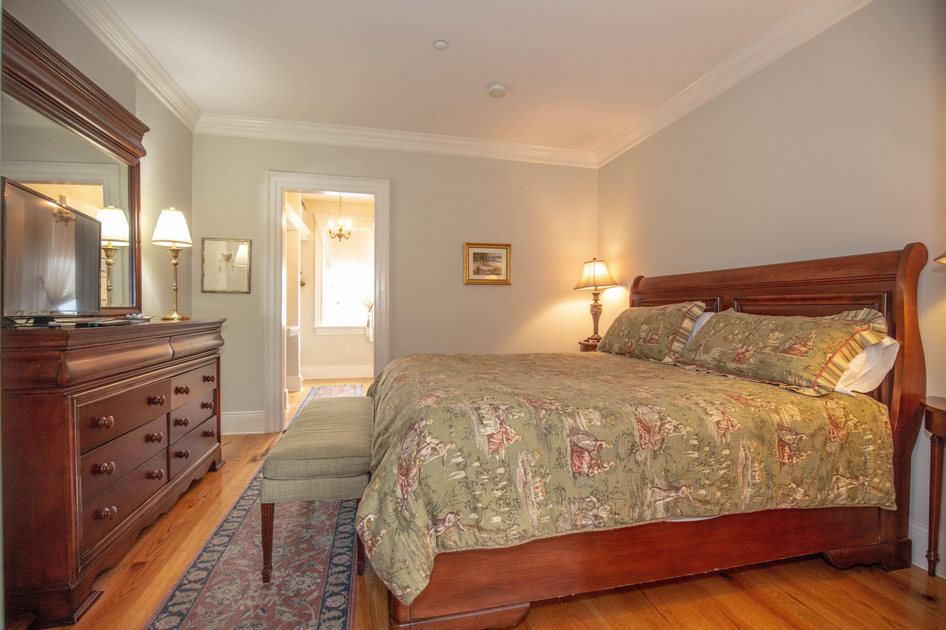 A bedroom with a wooden bed, a dresser, a mirror, and a door leading to another room.