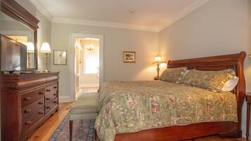 A bedroom with a wooden bed, a dresser, a mirror, and a door leading to another room.