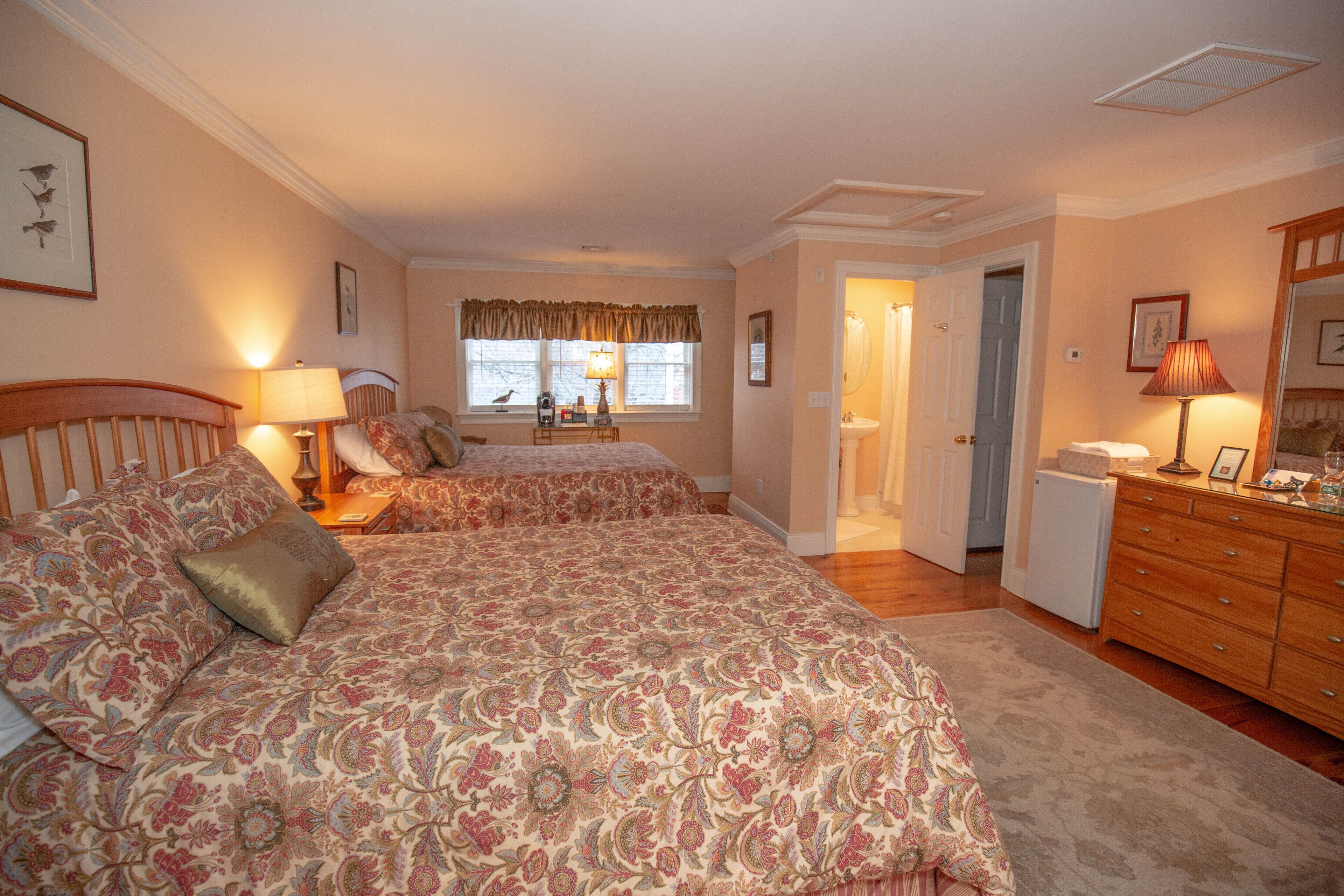 Een slaapkamer met twee bedden, een kaptafel, een dressoir en een raam met gordijnen.
