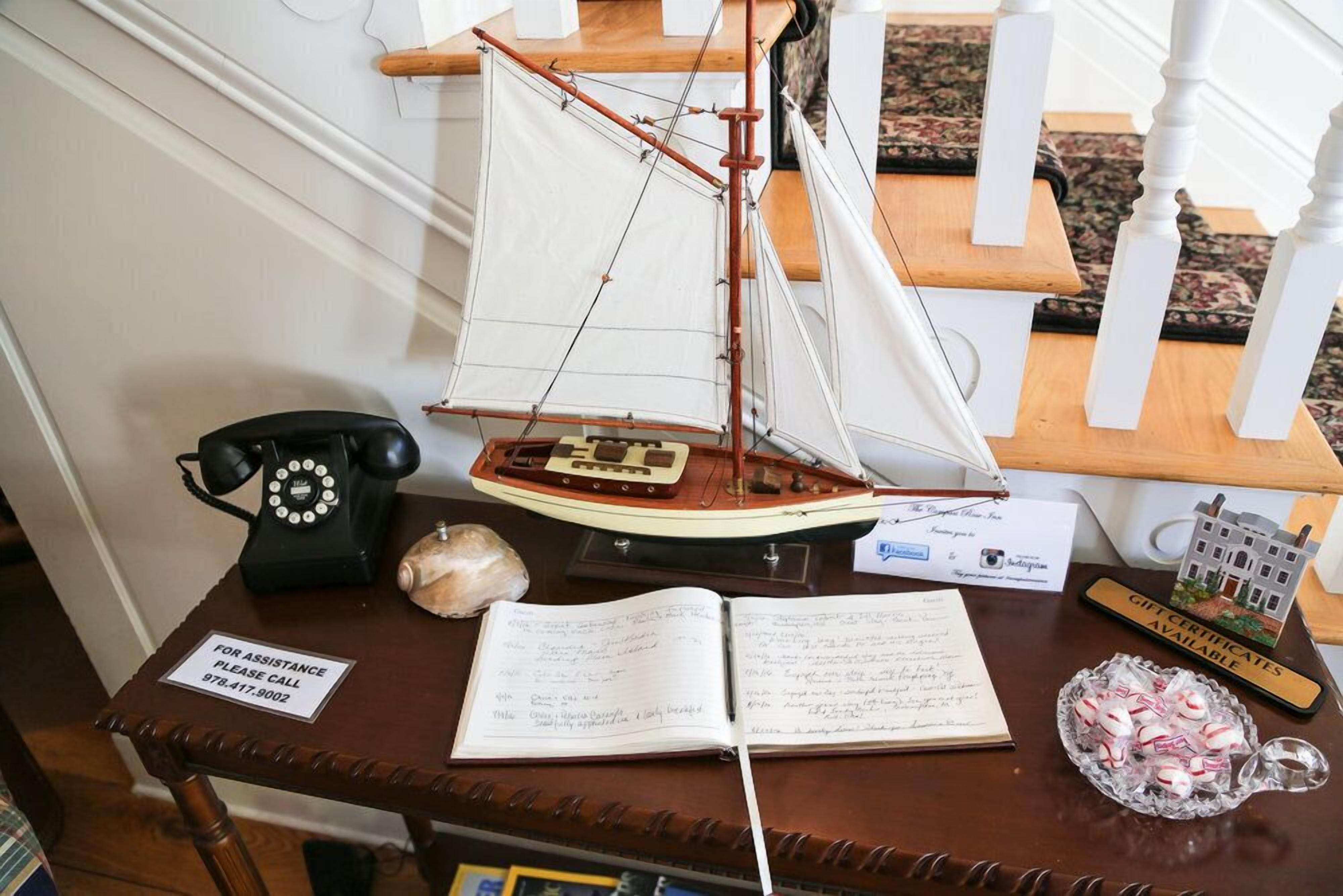 A wooden desk with a model sailboat, a telephone, a notebook, a gift certificate, and a small bowl of candies.