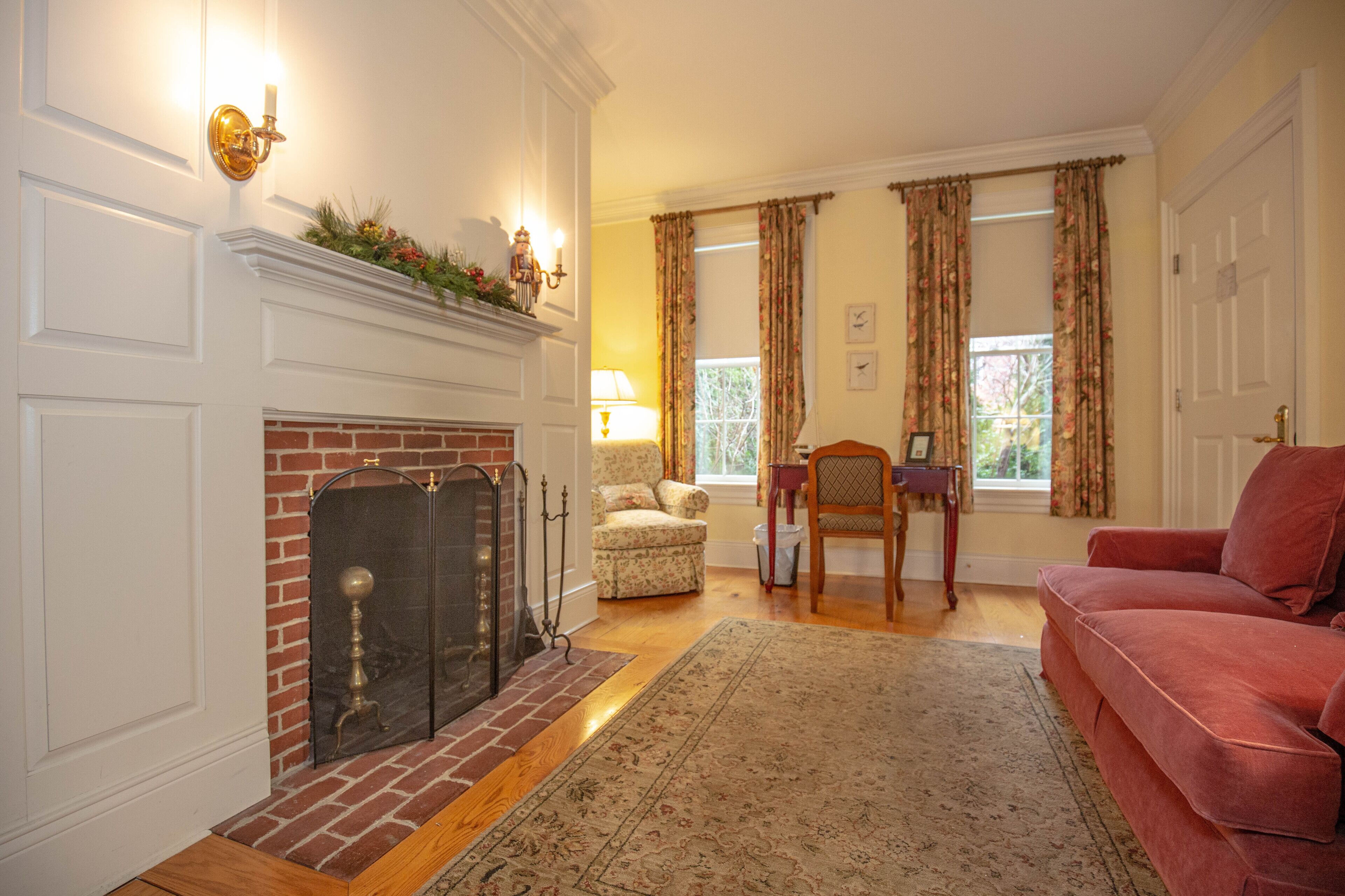 A living room with a fireplace, a red sofa, a patterned armchair, and a wooden floor.