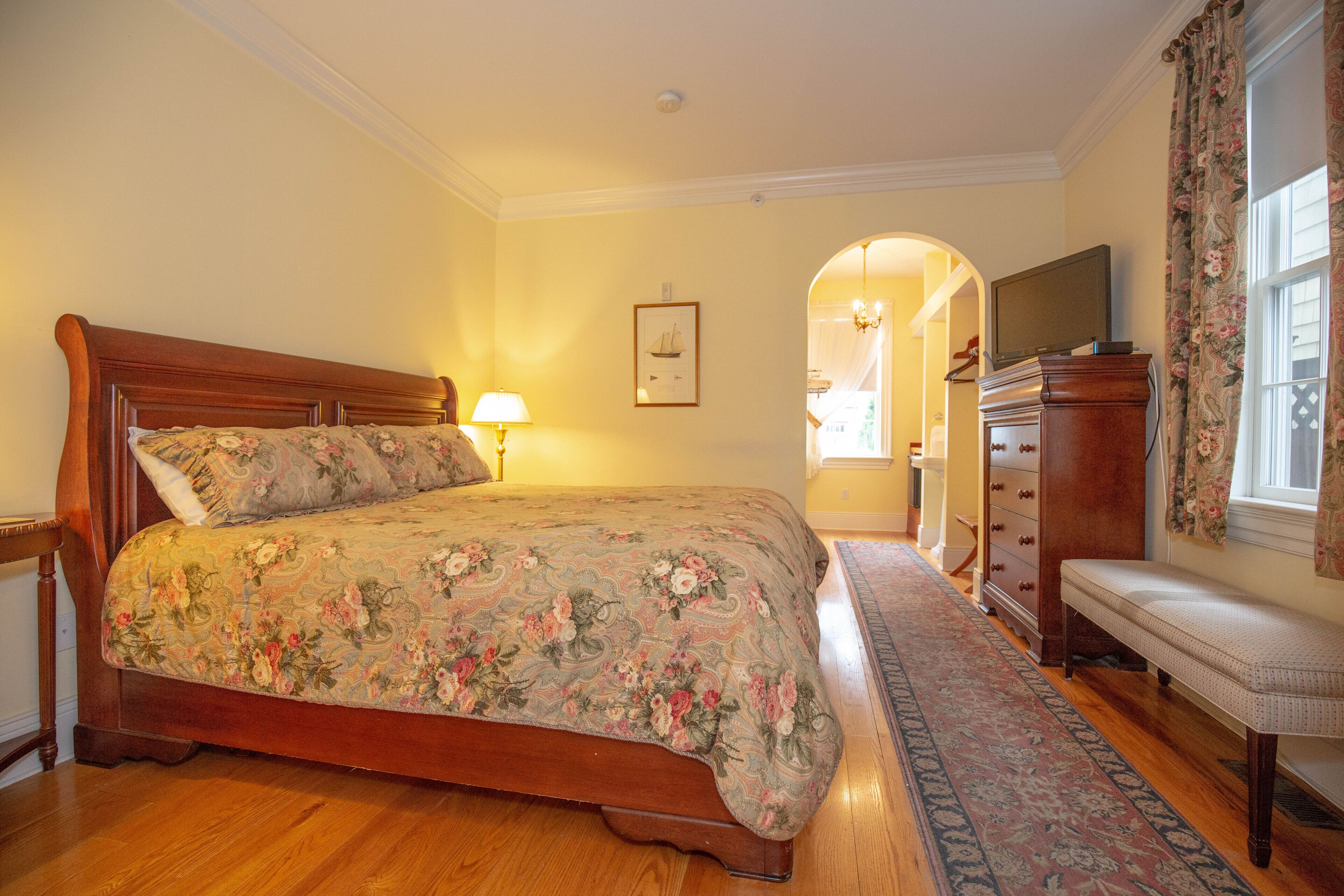 Een slaapkamer met een houten bed, nachtkastje, dressoir en een televisie op een standaard.