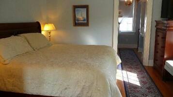 A bedroom with a large bed, a nightstand with a lamp, a framed picture on the wall, and a wooden dresser.