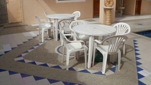 A poolside area with white plastic tables and chairs, a tiled floor with a geometric pattern, and a statue on a pedestal. - Hotel Francisco I (Salinas)