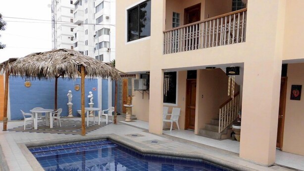 A swimming pool with a thatched roof seating area, a staircase, and a two-story building with balconies. - Hotel Francisco I (Salinas)