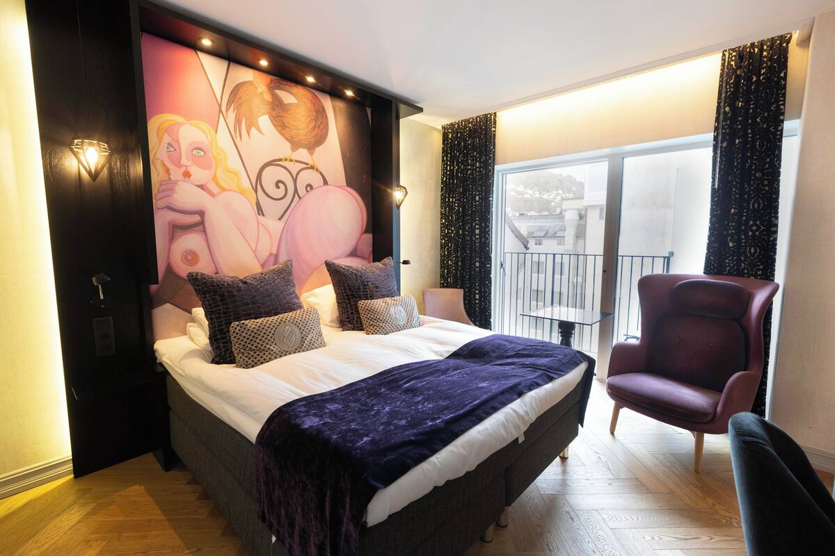 Un dormitorio con una cama grande, una silla, un mural en la pared y vistas al balcón.