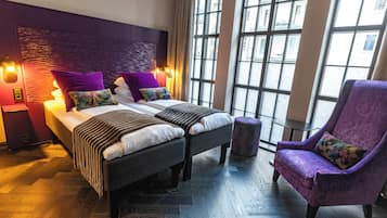 A modern hotel room with a large bed, two bedside tables, a purple armchair, and a view through large windows.
