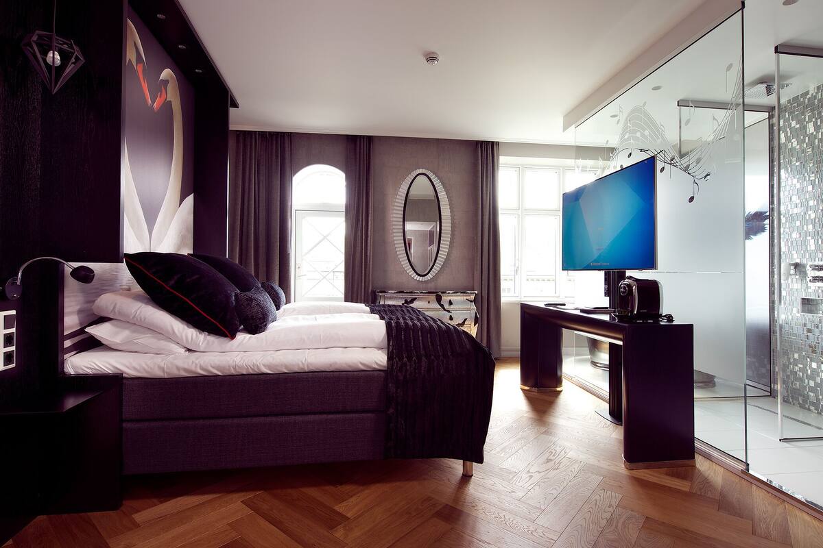 Un dormitorio moderno con una cama grande, un escritorio, un televisor y una zona de ducha con mampara de cristal.