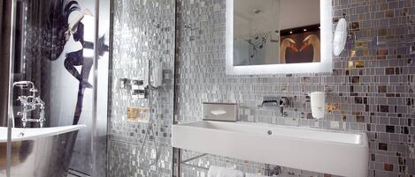 A modern bathroom with a glass shower enclosure, a white sink, and a mirror with a mosaic backsplash.