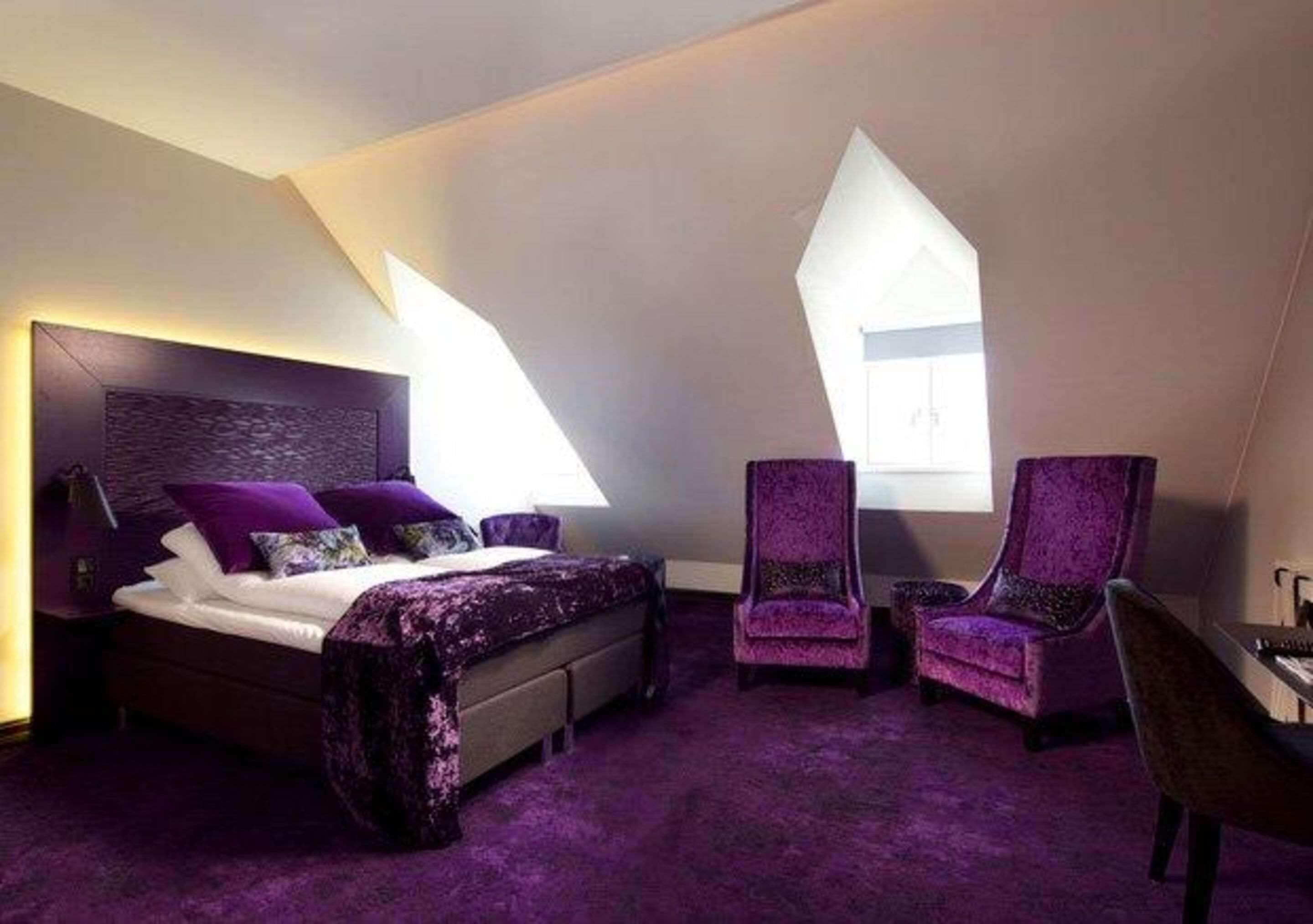 A bedroom with a bed, two chairs, a desk, and a large window.