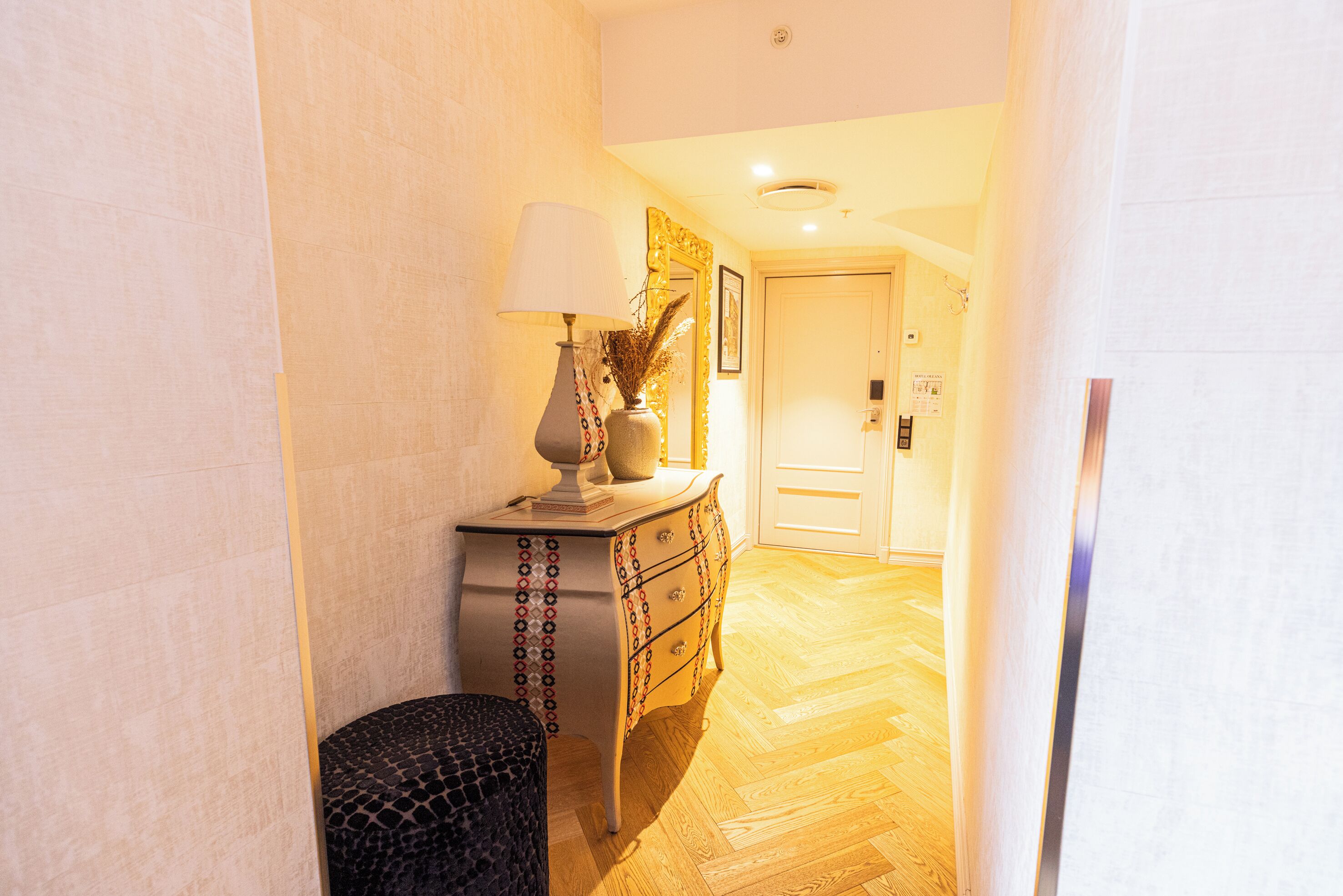 A hallway with a wooden floor, a lamp, a decorative vase, and a door.