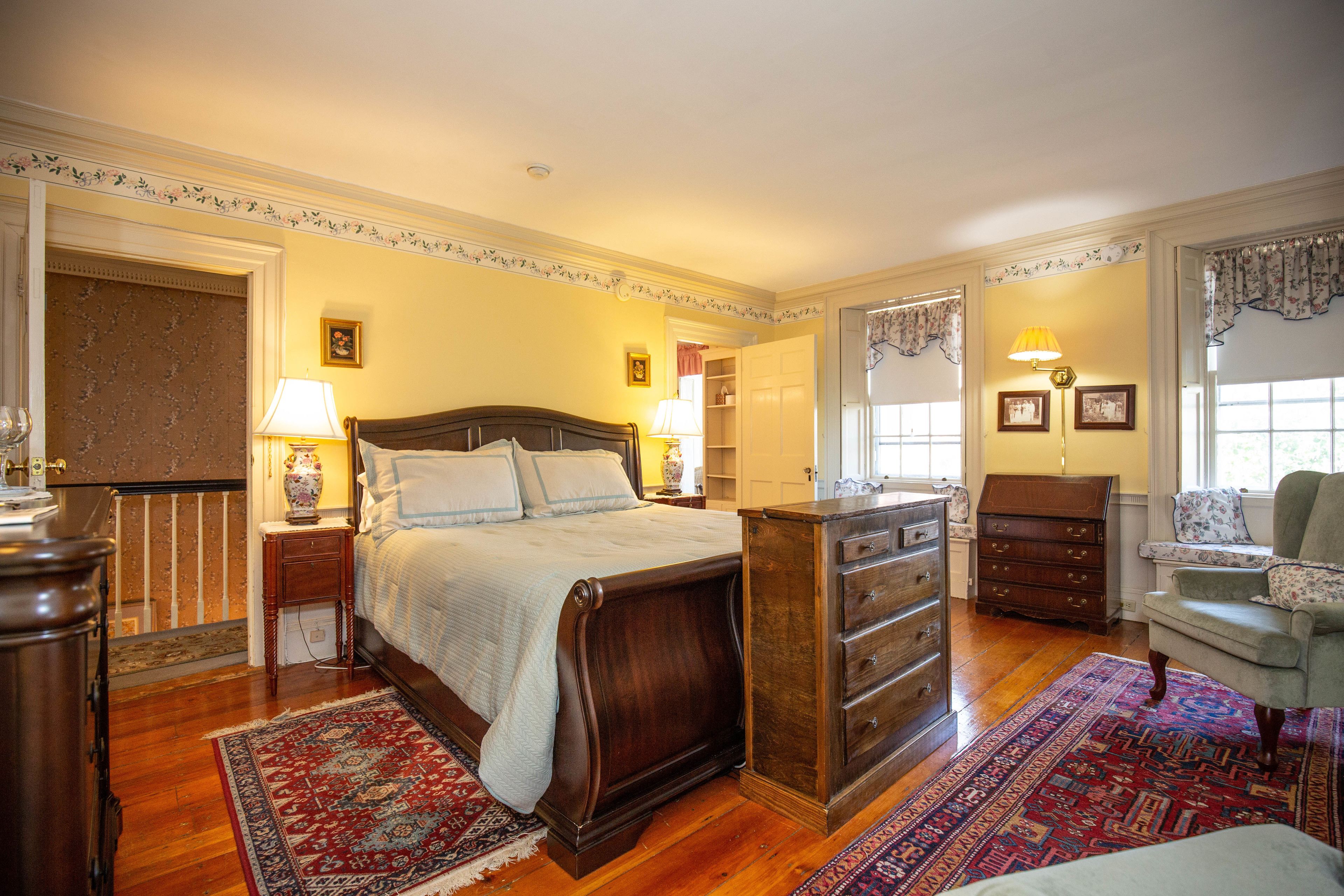 Un dormitorio tradicional con una cama grande, cómoda de madera y una silla.