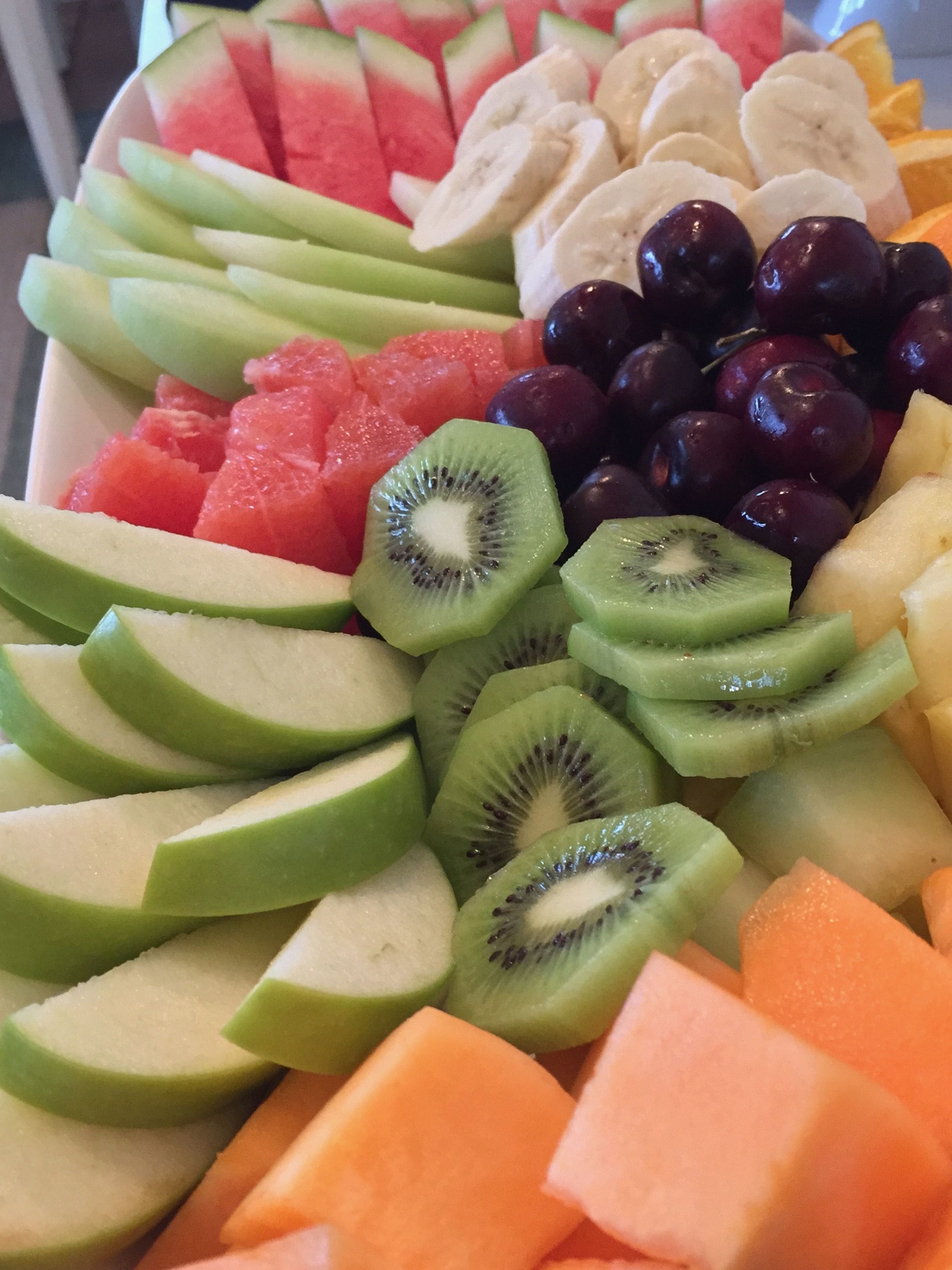 Una bandeja de frutas con diversas frutas cortadas, como sandía, kiwi, uvas y melón.