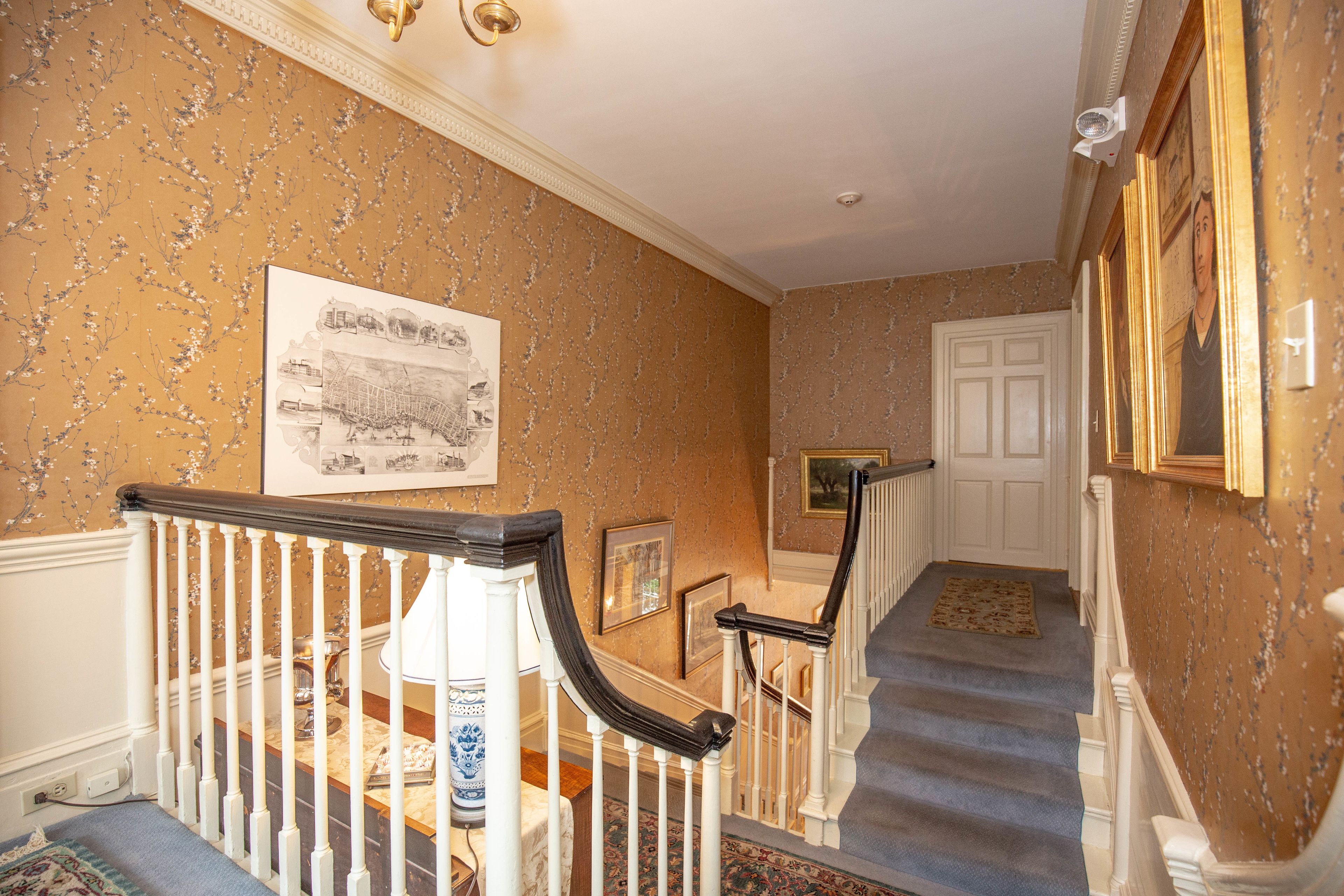 A staircase with a carpeted landing, a white door, and a wall with floral wallpaper.