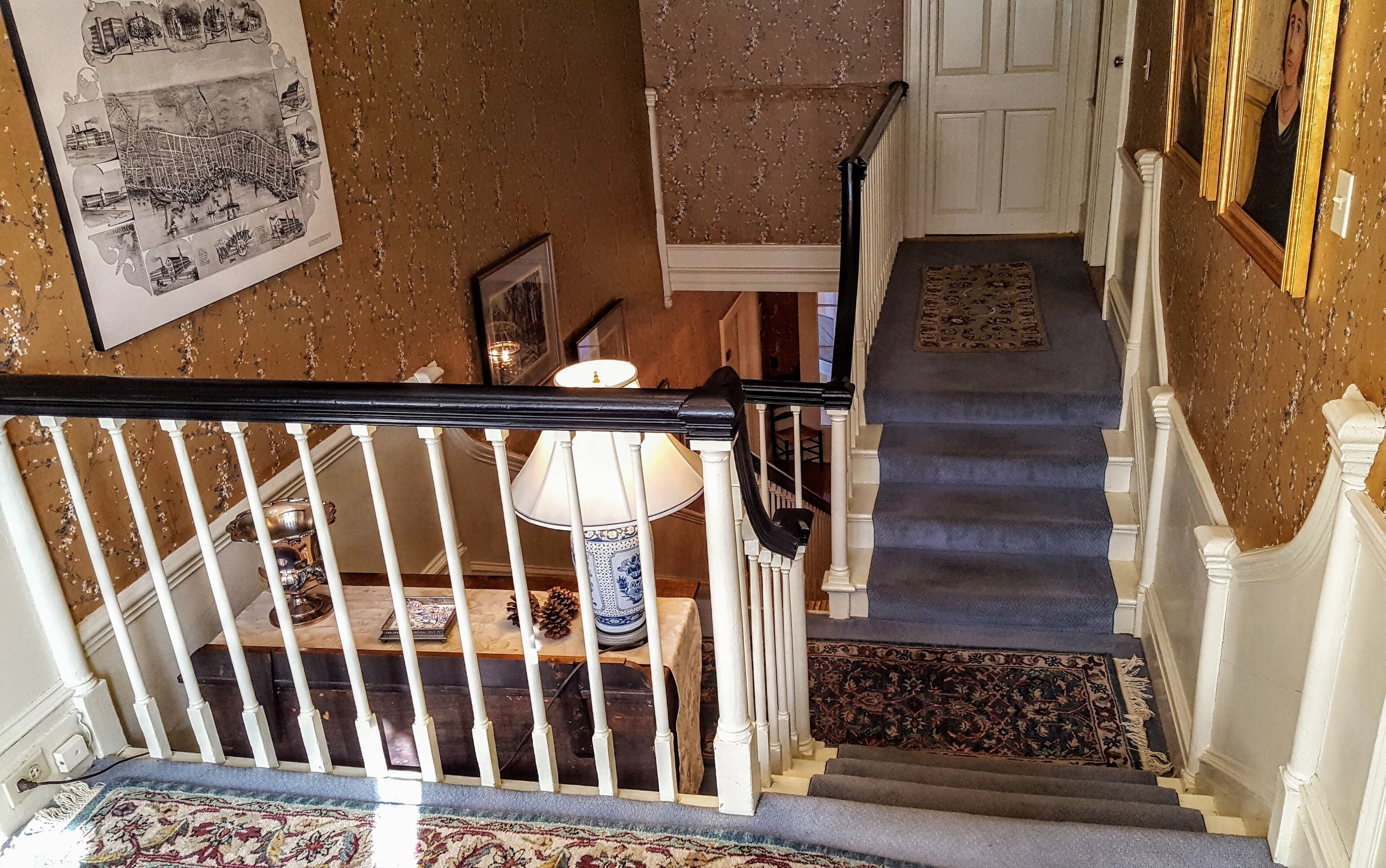 A staircase with a black handrail, white balusters, and a patterned carpet.