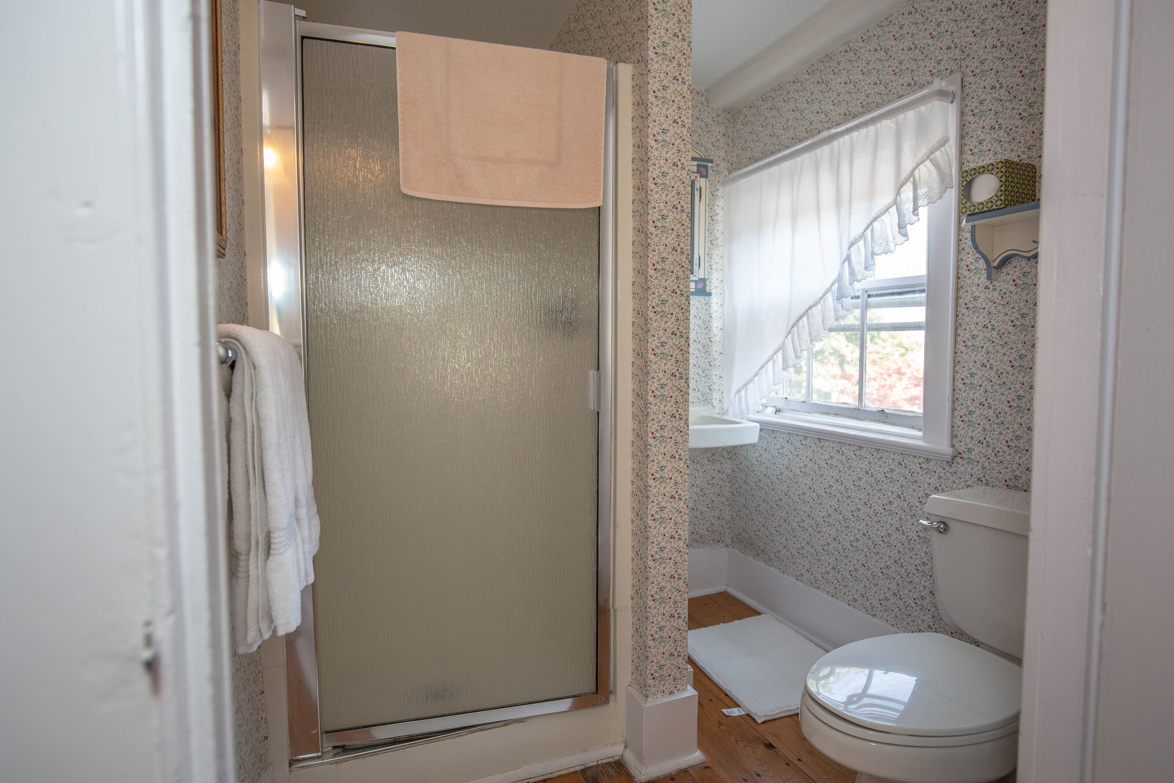 A bathroom with a shower, toilet, and window.