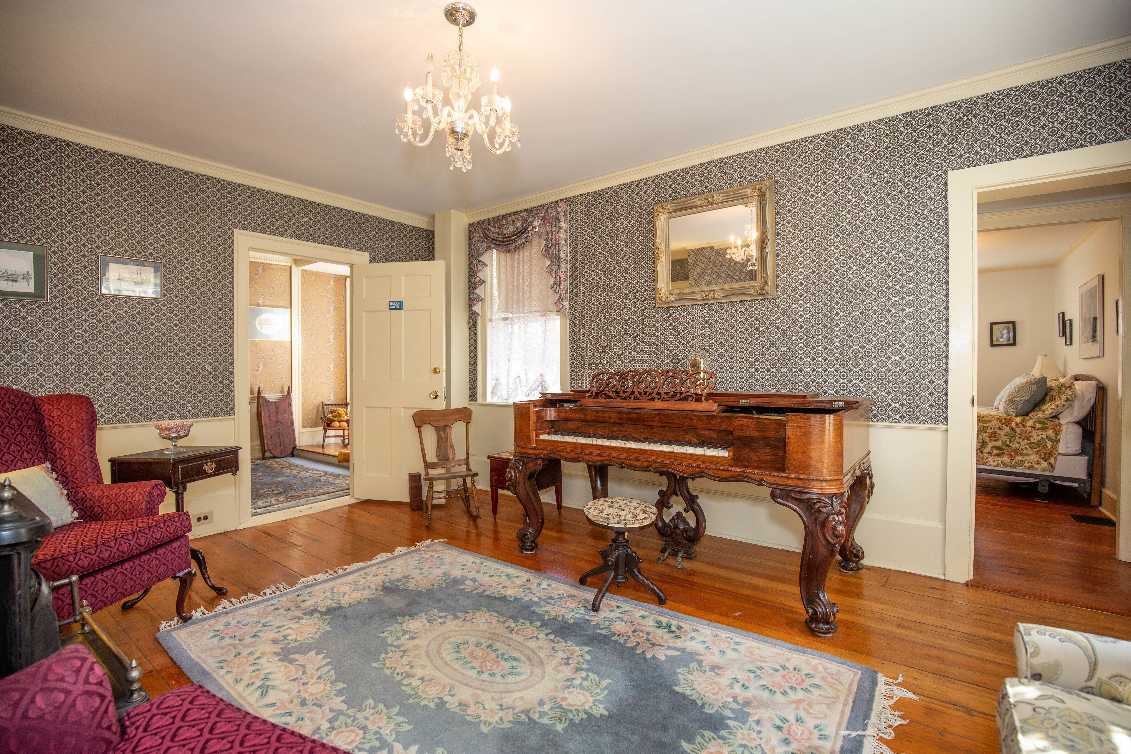 Un salon avec un grand piano, un fauteuil rouge et un tapis à motifs.