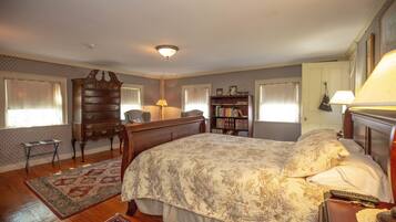 A bedroom with a large bed, a wooden dresser, a bookshelf, and a desk with a lamp.