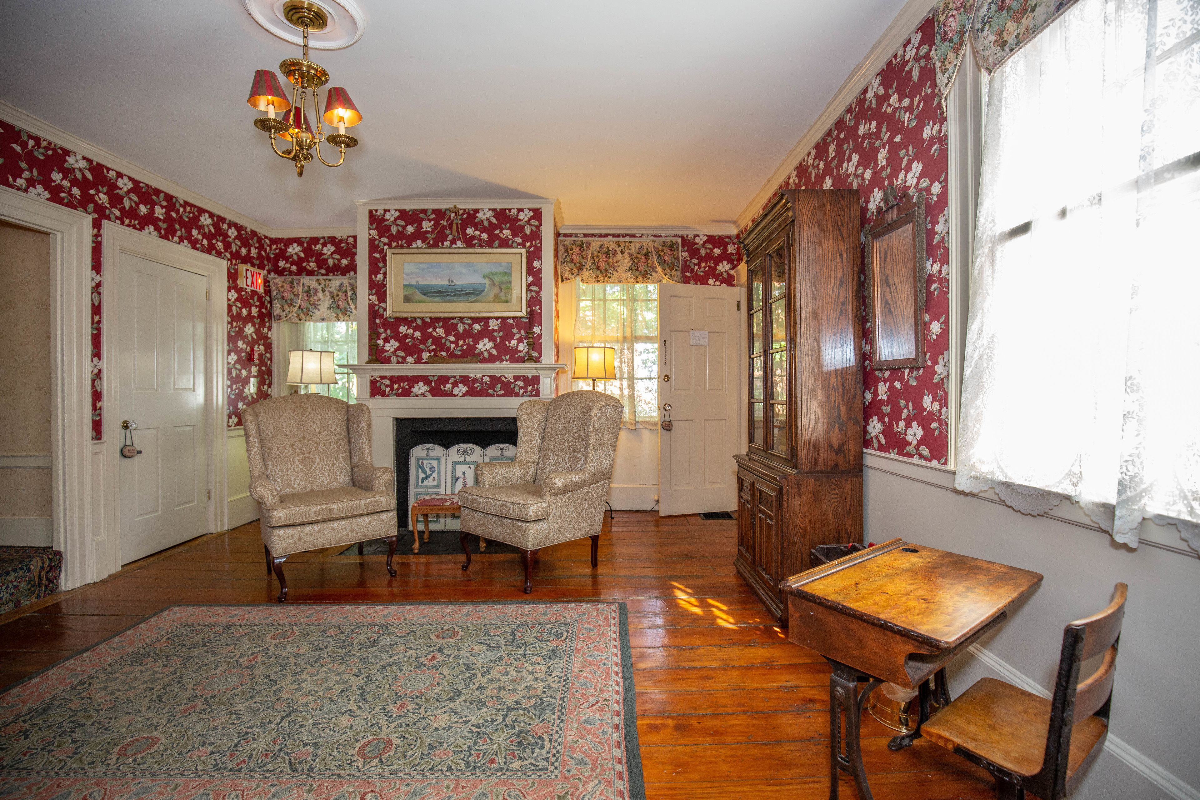 A room with two armchairs, a wooden table, a patterned rug, a fireplace, and floral wallpaper.