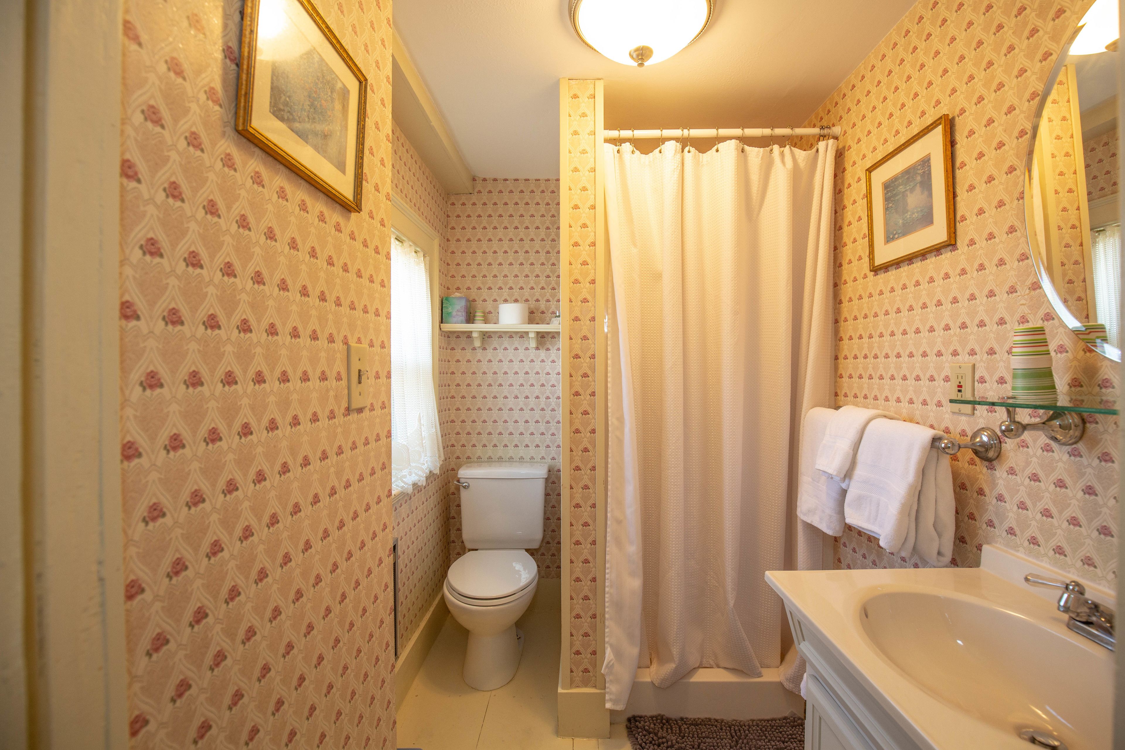 A bathroom with a toilet, sink, and shower curtain. There are framed pictures on the wall and a towel rack.