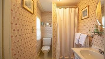 A bathroom with a toilet, sink, and shower curtain. There are framed pictures on the wall and a towel rack.