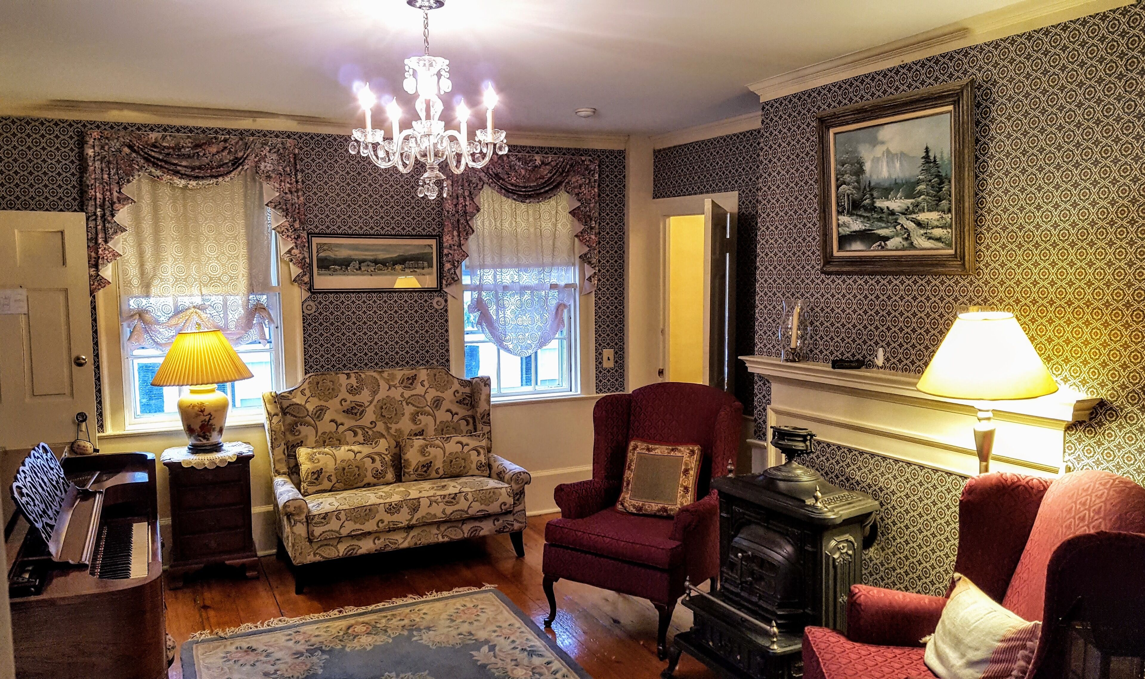 A traditional living room with patterned wallpaper, a chandelier, a fireplace, and a vintage stove.