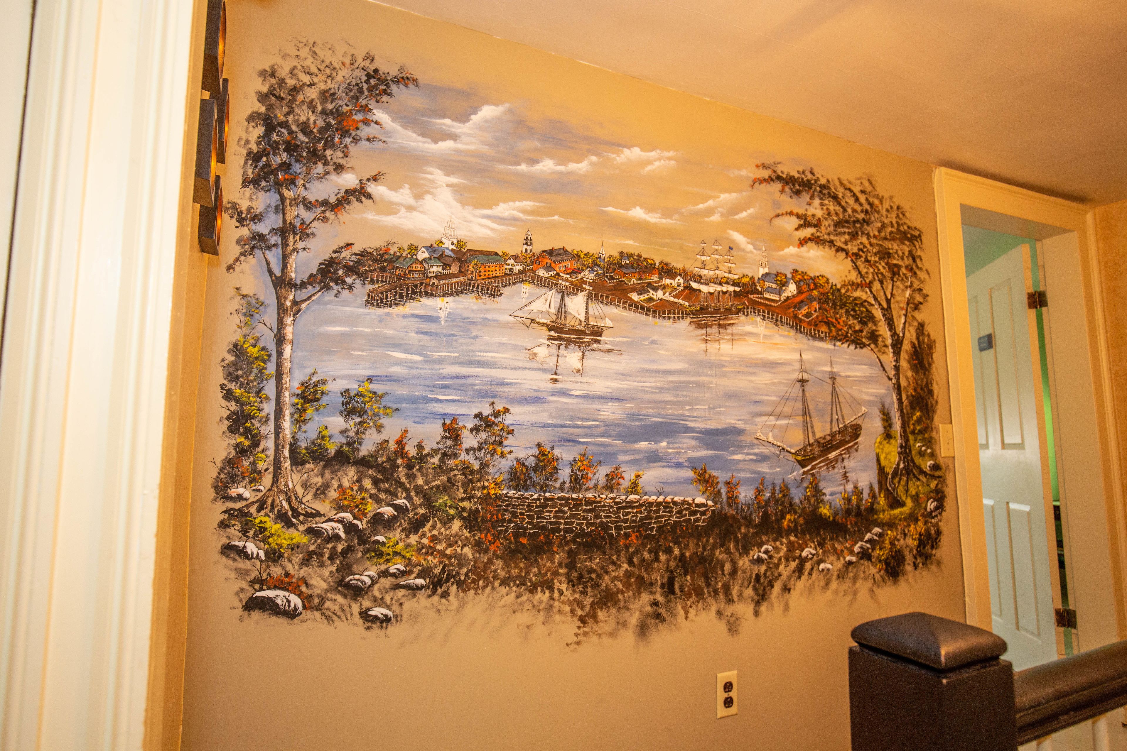 A mural of a coastal scene with ships, trees, and a stone wall.