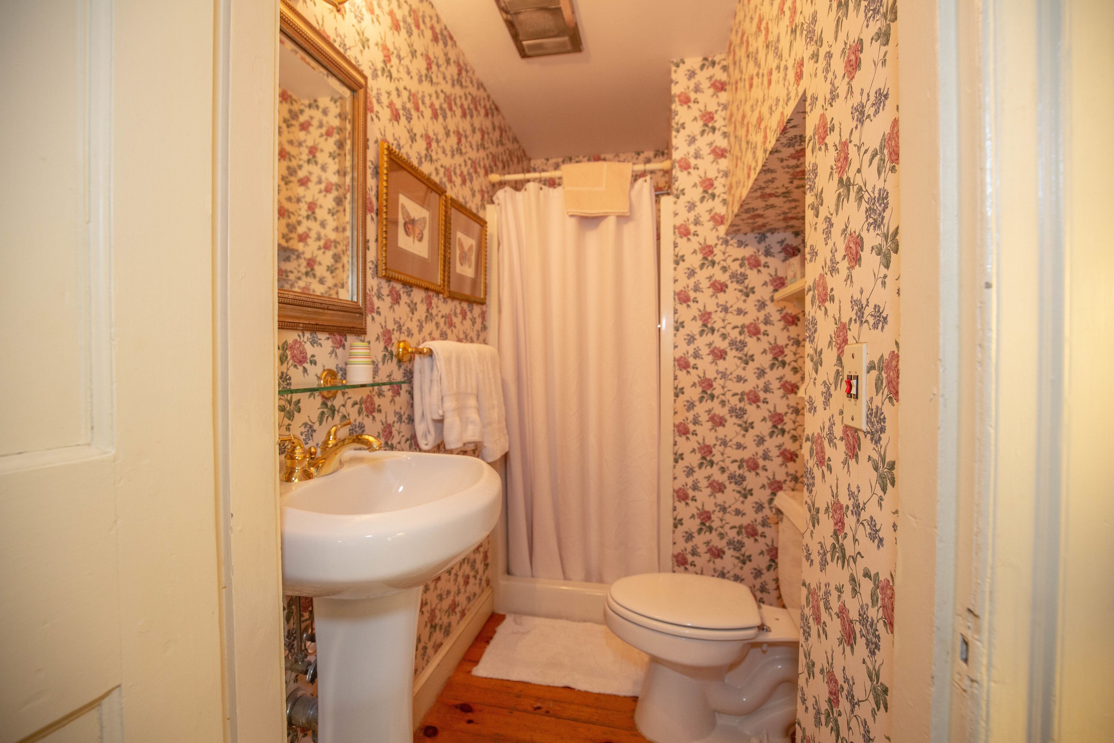 A bathroom with floral wallpaper, a white sink, a toilet, and a shower curtain.