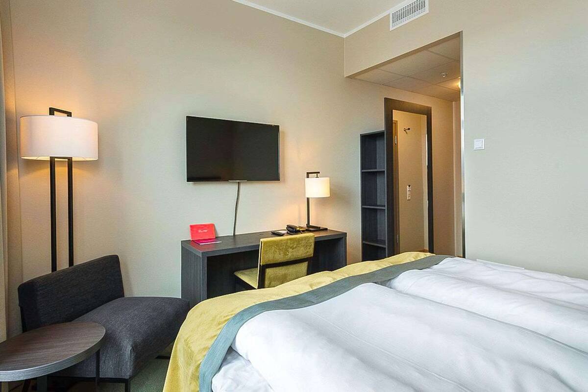 A hotel room with a bed, desk, chair, TV, and a small table.
