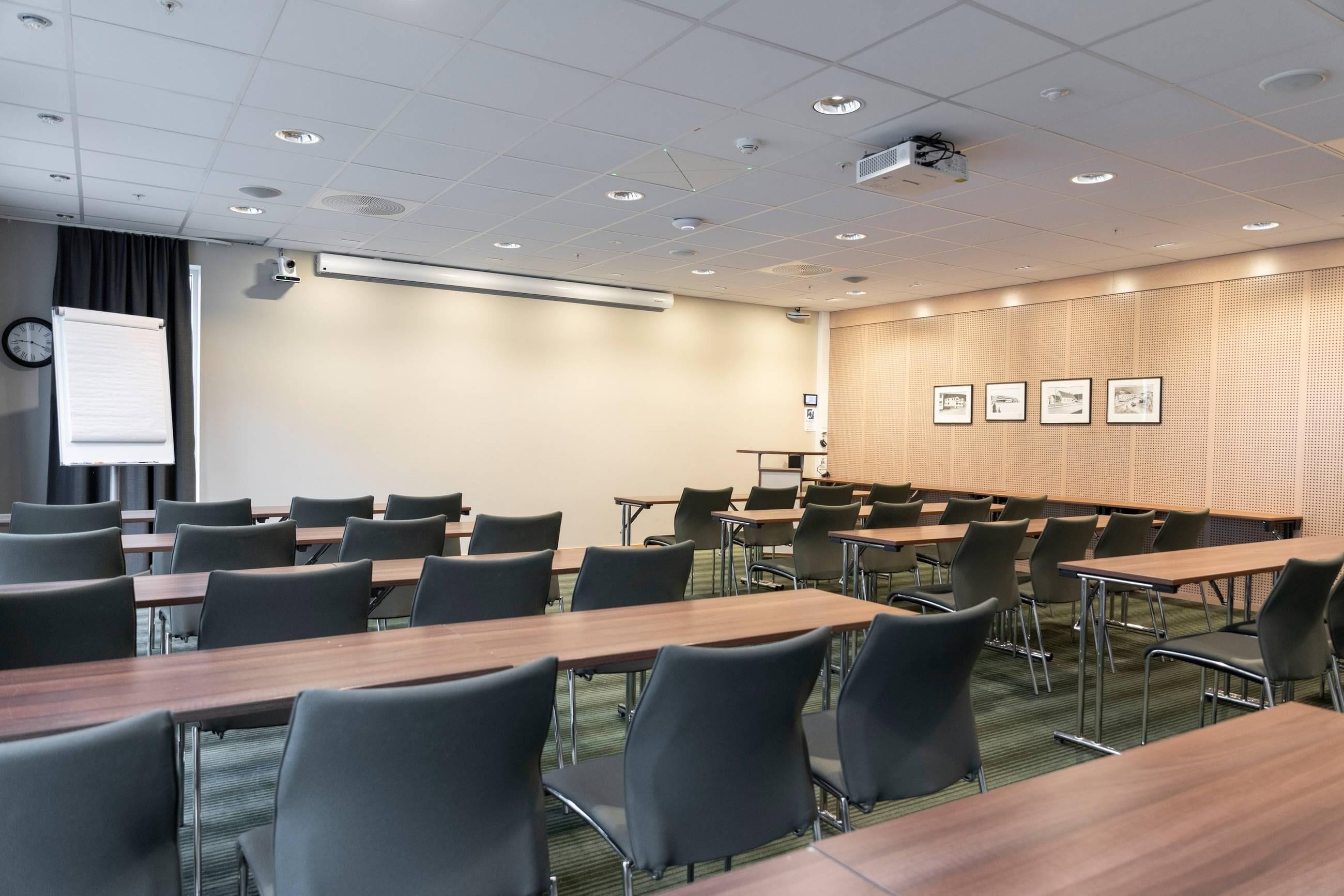 Un salón de conferencias con mesas, sillas, un proyector y una pizarra.