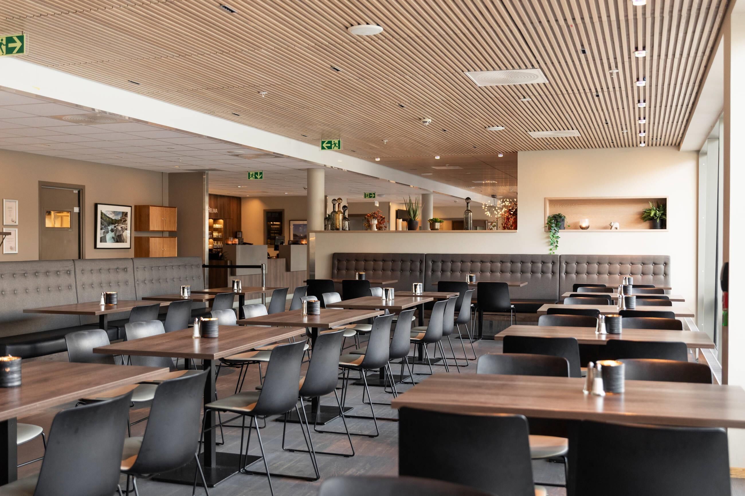 A modern restaurant with long tables, black chairs, and a wooden ceiling.