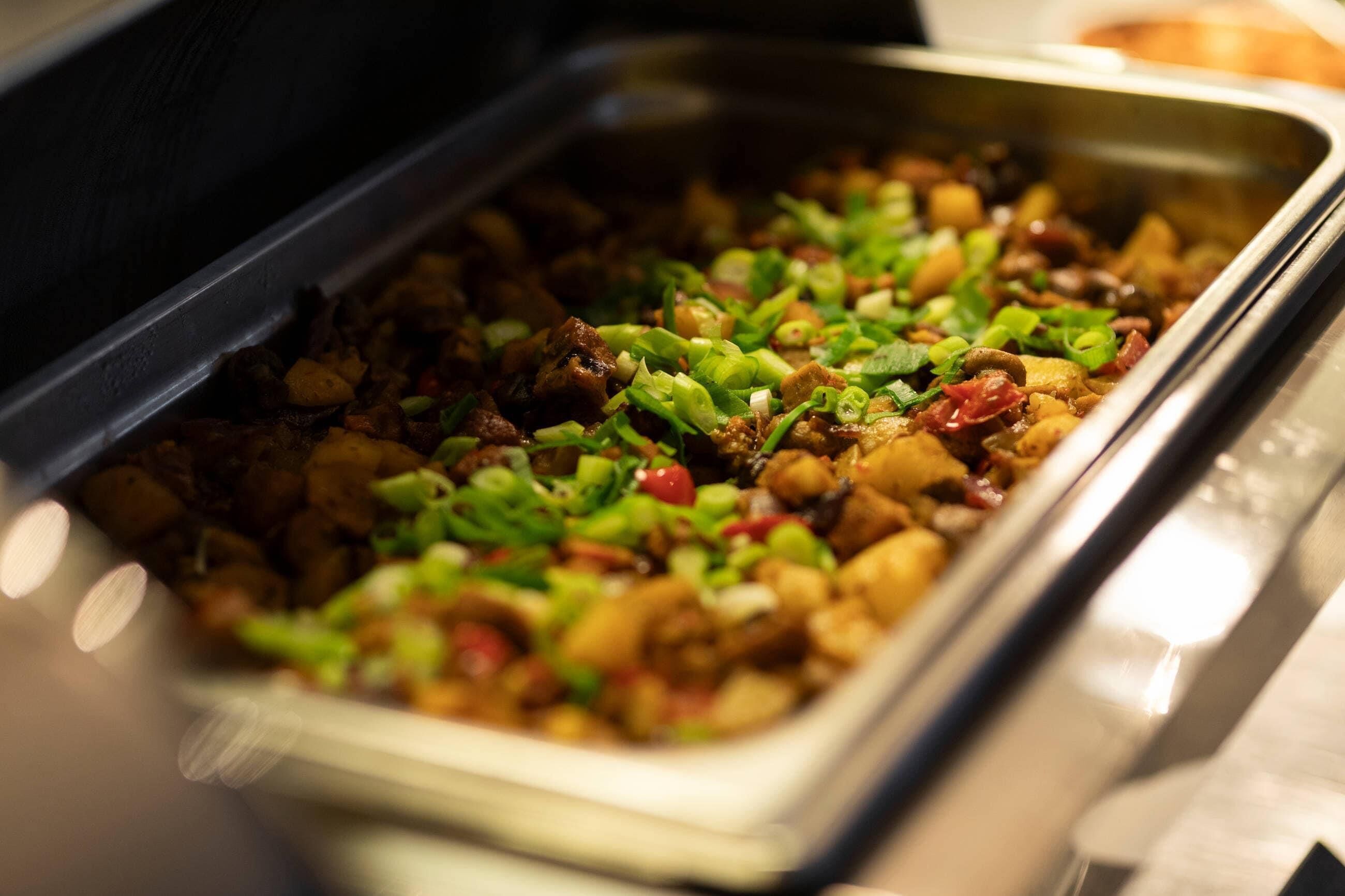 A buffet with a variety of dishes, including what appears to be a meat-based dish garnished with green herbs and diced vegetables.
